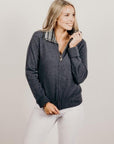 A woman smiling, wearing a gray Merinosilk knitted jacket with a striped collar, and white pants.