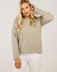 Woman wearing a beige sweater and white pants against a plain background