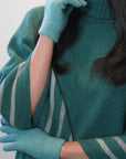 Person wearing a teal sweater and matching gloves against a white background
