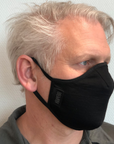Man wearing a black travel mask with adjustable elastic straps, made from merino soft & comfort next to skin, with a label showing 'Made in New Zealand', and highlighting features such as 100% breathable, adjustable elastic straps, and a machine washable filter.