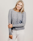 Woman wearing a gray cardigan and white pants against a plain background