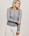 Woman wearing a gray cardigan and white pants against a plain background