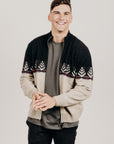 A person standing against a plain background, wearing a Merinosilk Silver Fern Jacket with full zip and ribbed hems, featuring a unique Silver Fern print.
