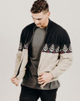 Man wearing a black and beige patterned sweater over a gray shirt on a plain background