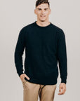 Man wearing a navy sweater and beige pants against a plain backgroundnavy
