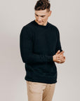 Man wearing a navy sweater and beige pants against a plain background