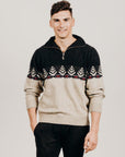A man wearing a Merinosilk Silver Fern zip Sweater with a half-zip front, paired with black trousers. The sweater has a silver fern pattern on a beige background.