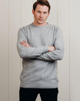 Man wearing a gray sweater with arms crossed against a light wooden panel background