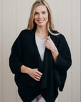 Woman wearing a black cardigan over a white top against a light background