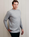 Man wearing a gray sweater against a light wooden panel background