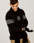 Man wearing a black sweater with white stripes and a scalf and matching gloves on a plain background