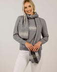 Woman wearing a gray sweater and patterned scarf against a plain background