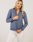 Woman wearing a blue zip-up sweater and white pants on a plain background