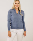 Woman wearing a blue zip-up sweater and white pants on a plain background