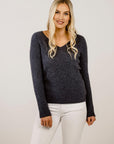 A woman wearing a dark ribbed sweater and white pants against a plain background