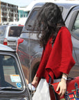 Person in a red sweater standing next to a car with a colorful bag.