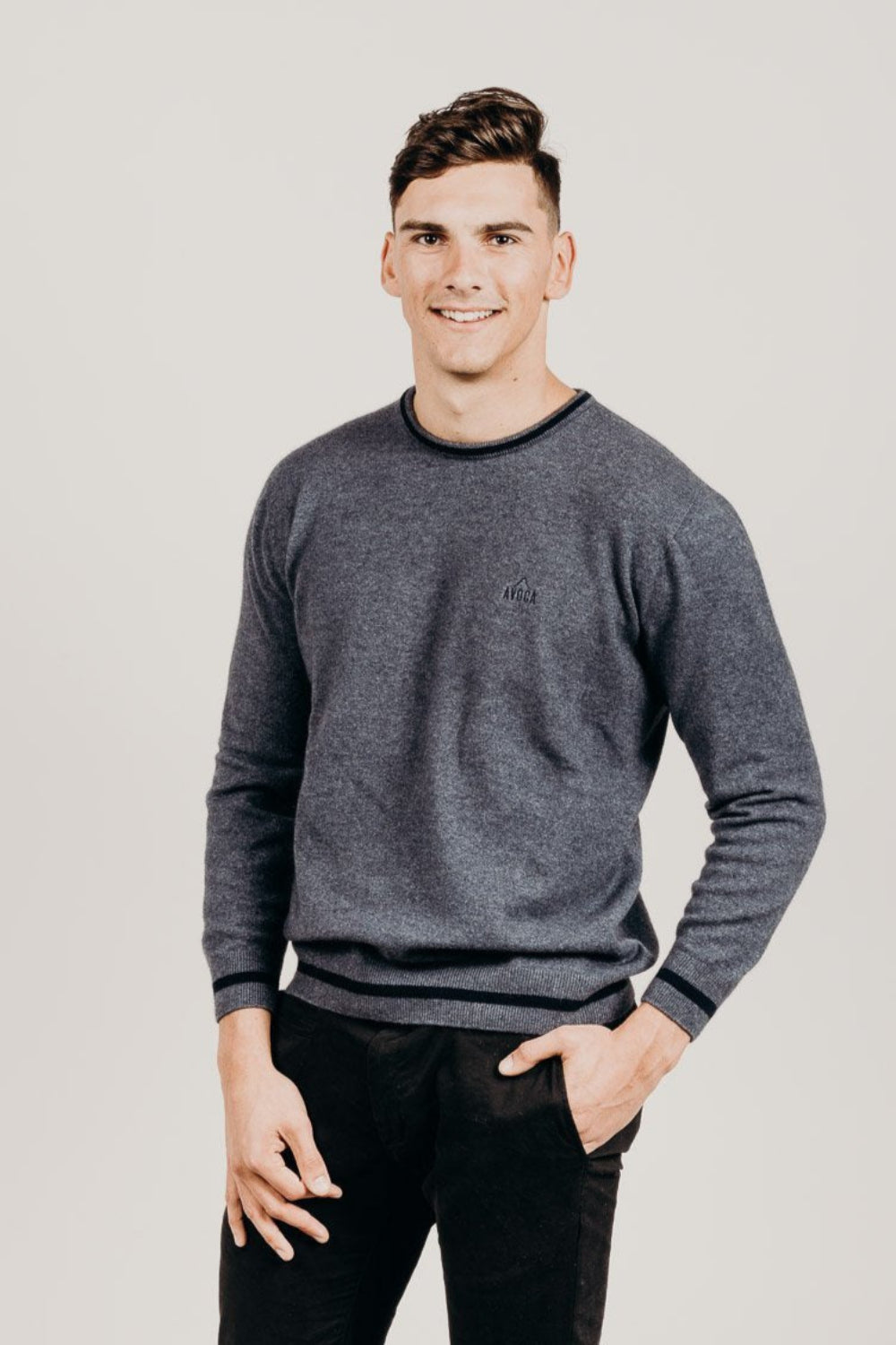 Man wearing a gray sweater and black pants against a plain background