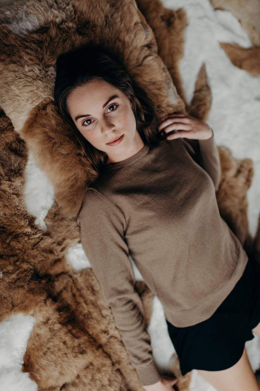 Woman in a brown sweater and black shorts lying on a fur rug