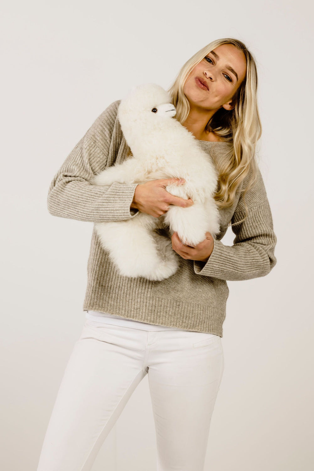Woman in lichen sweater holding a white fluffy toy against a plain background