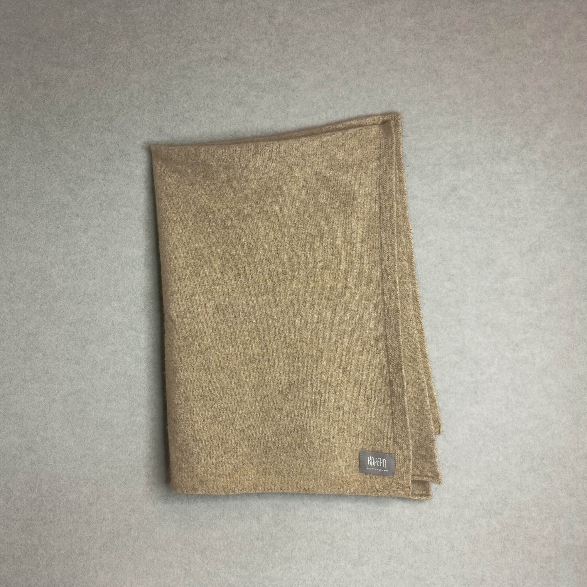 Beige baby blanket with a brand label on a gray background