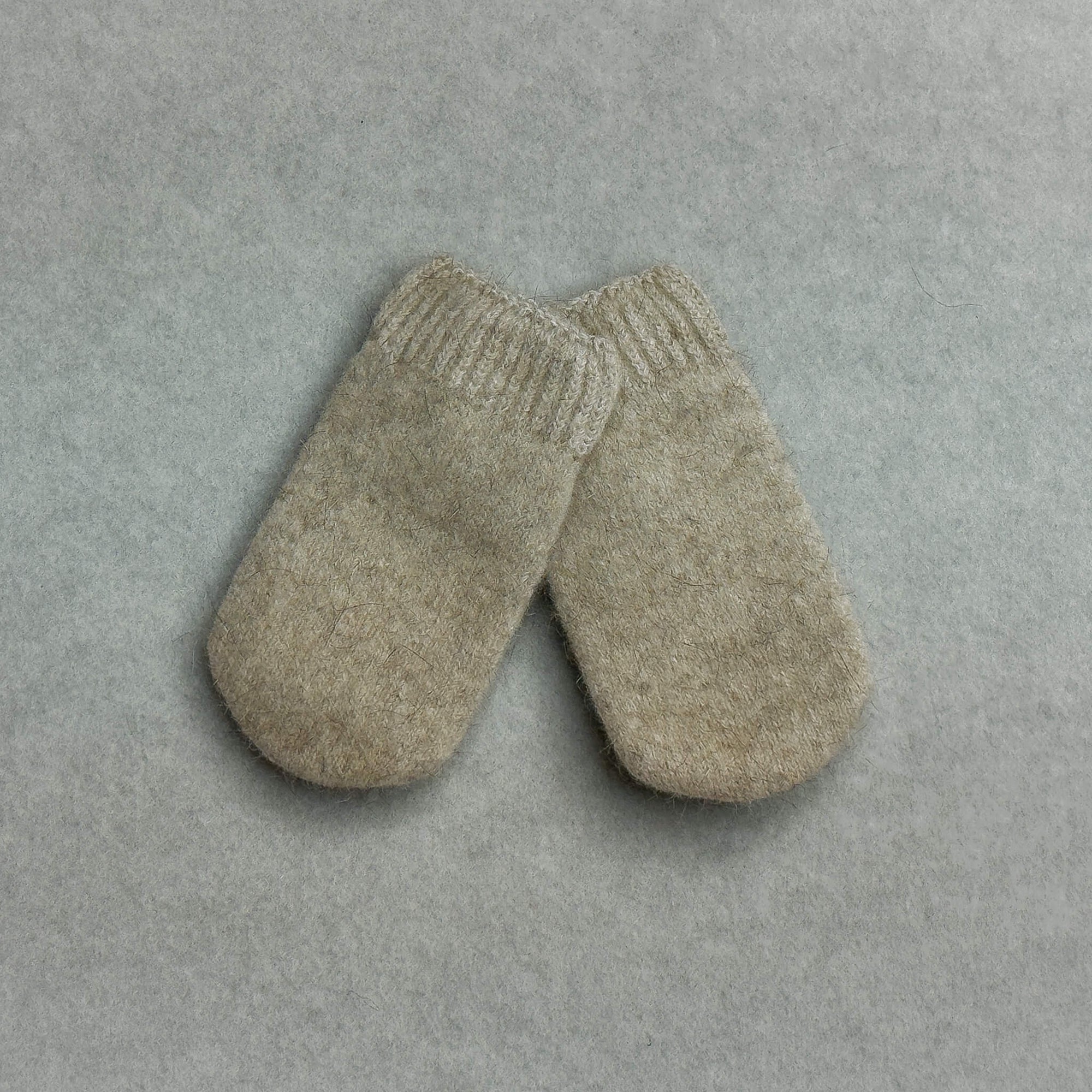 Pair of beige baby mittens on a gray background