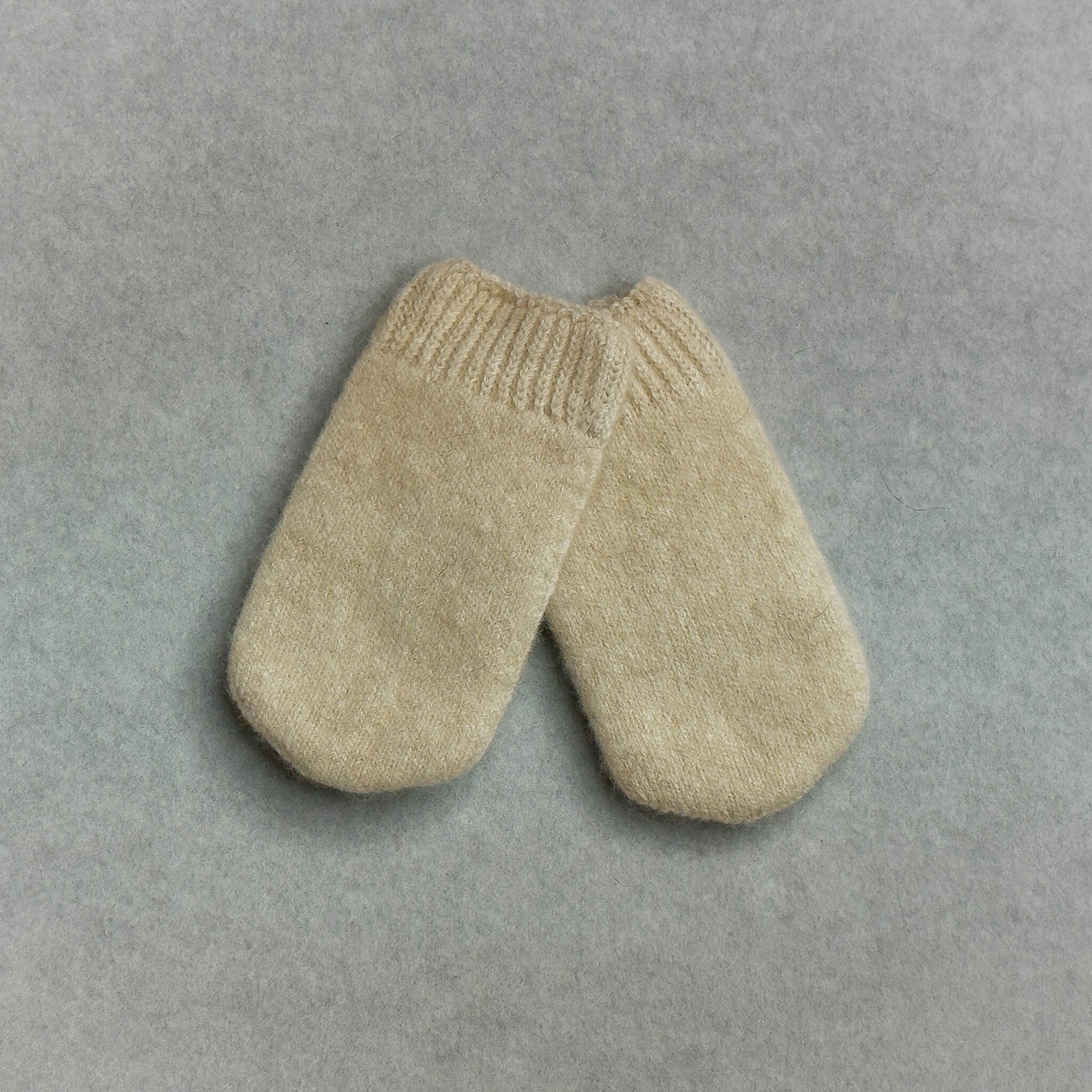 Pair of beige knitted baby mittens on a gray background