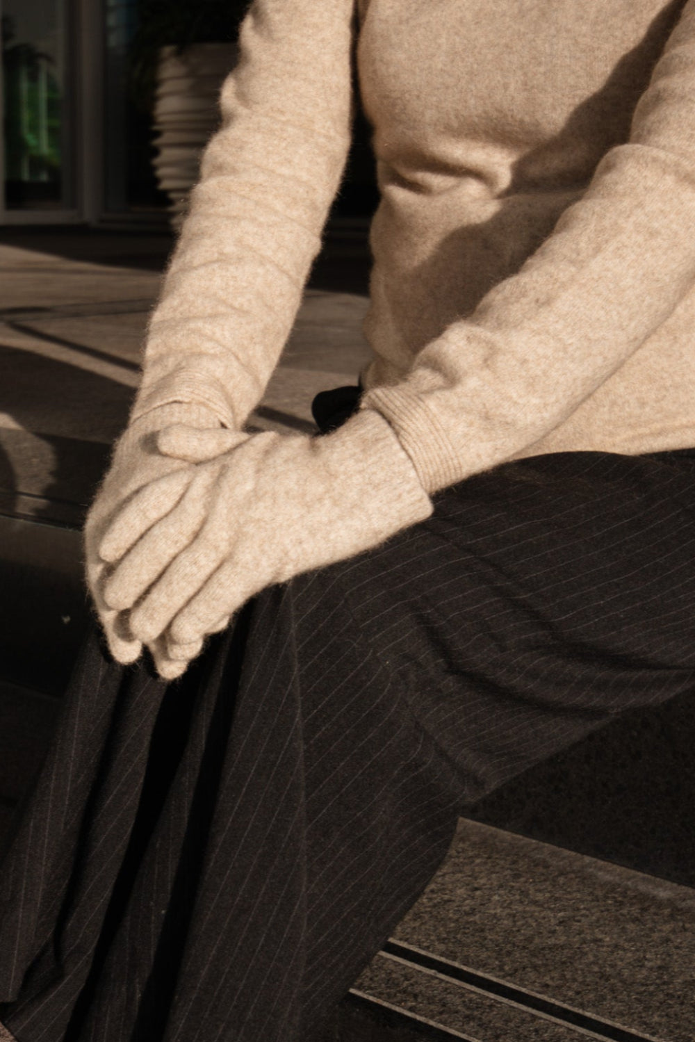 Person wearing a beige sweater, dark pants, and gloves sitting on steps.