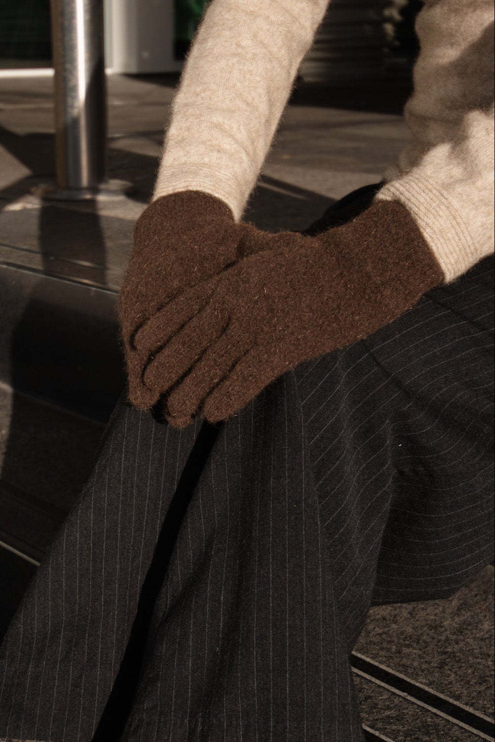 Person wearing brown gloves and dark pinstripe pants sitting on a black chair.