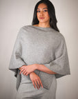 Woman wearing a gray poncho against a plain background