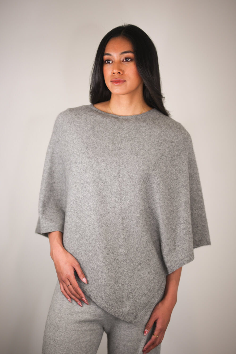 Woman wearing a gray poncho against a plain background