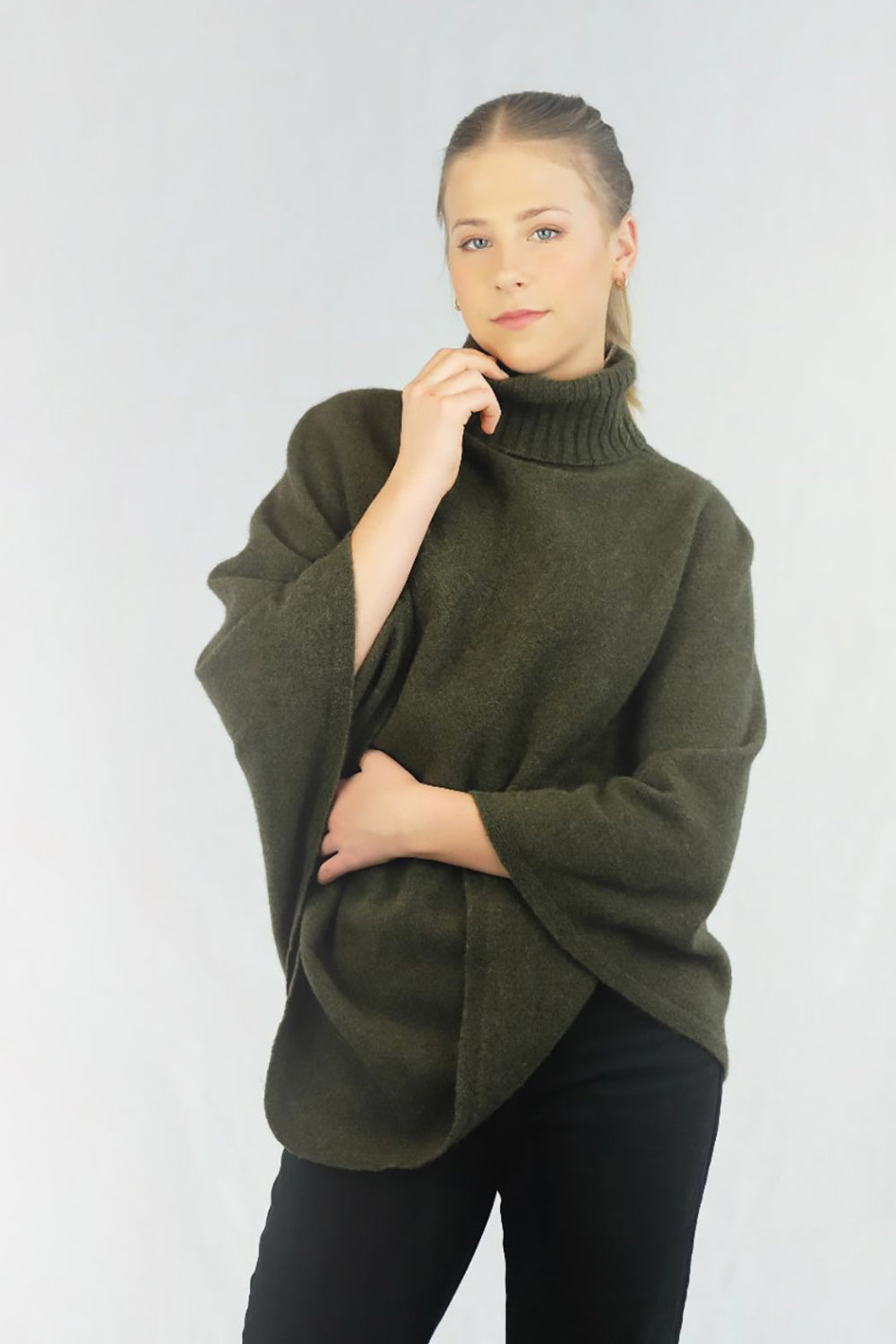 A woman wearing a green turtleneck Merinosilk rib neck plain poncho, paired with black pants.