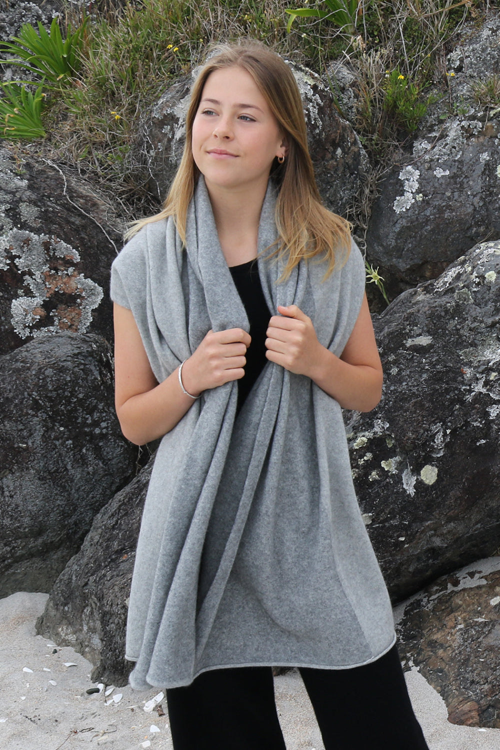 Woman wearing a gray wrap standing among rocks