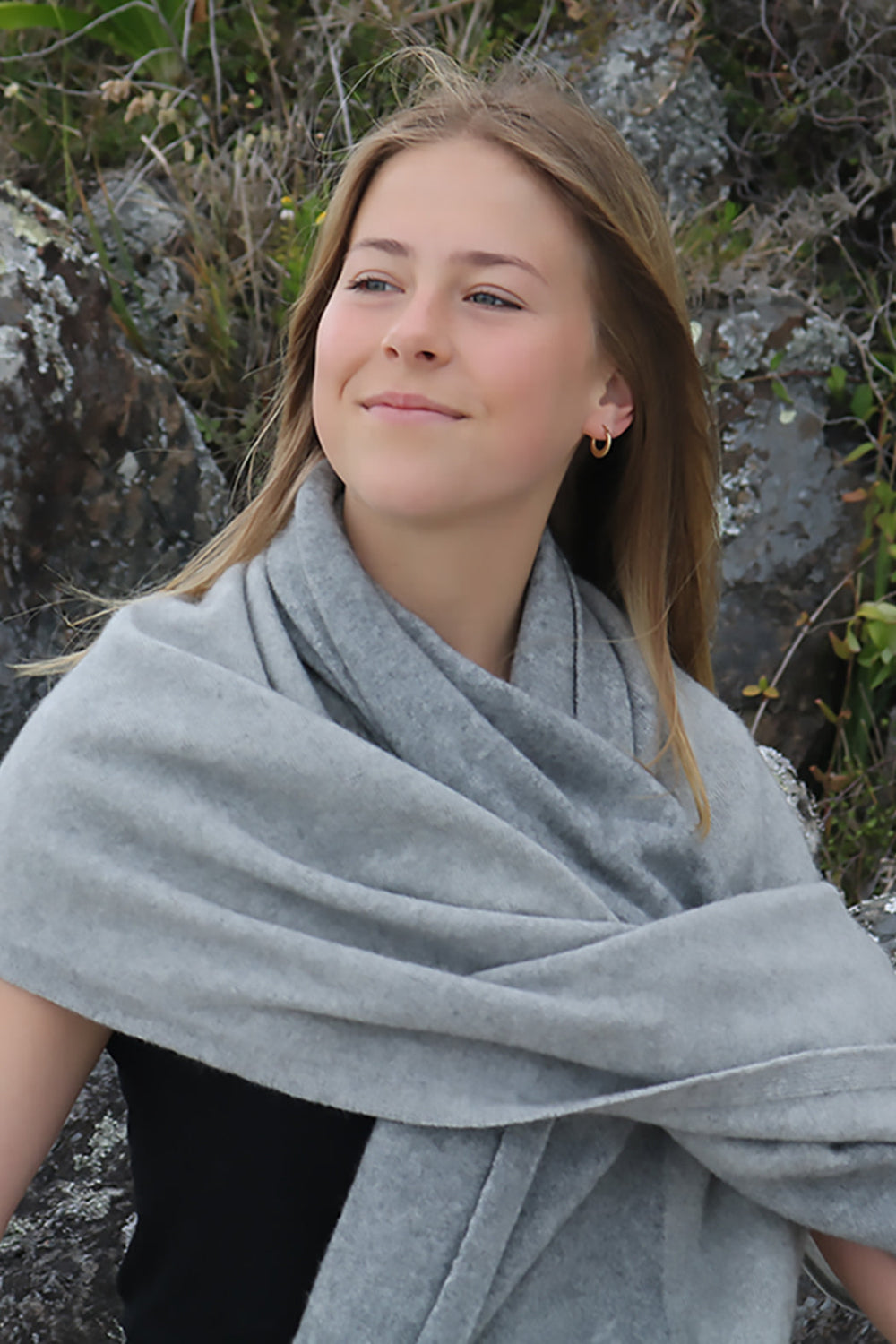 Woman wearing a gray shawl outdoors with rocks and plants in the background