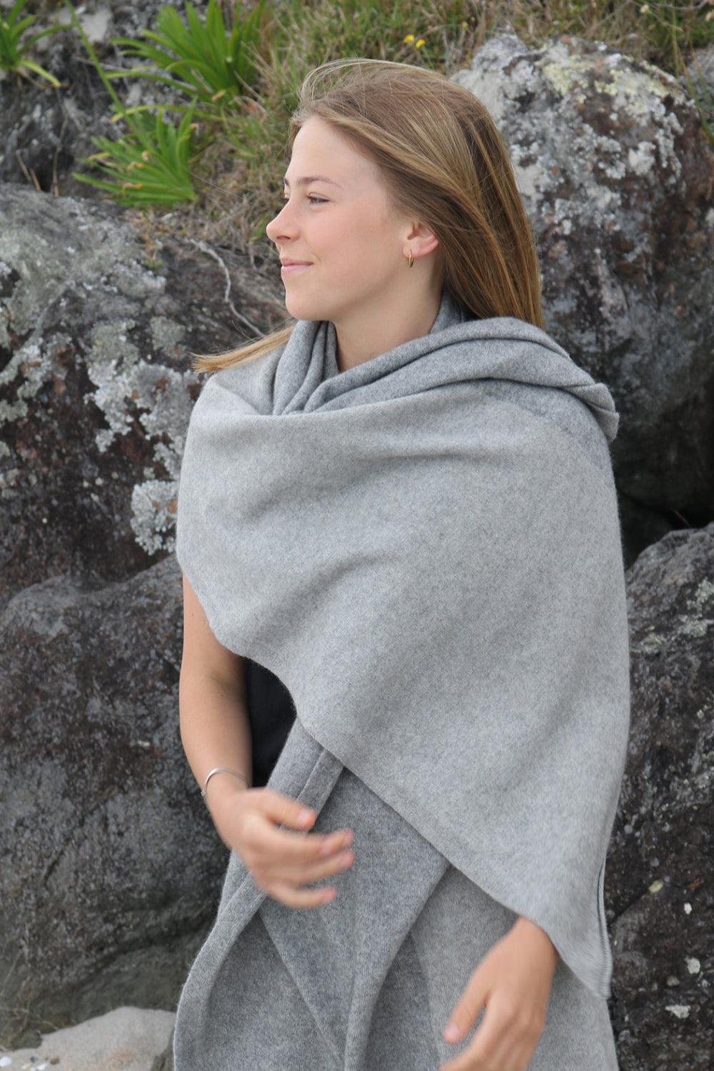 Woman wrapped in a gray stole standing against a rocky background