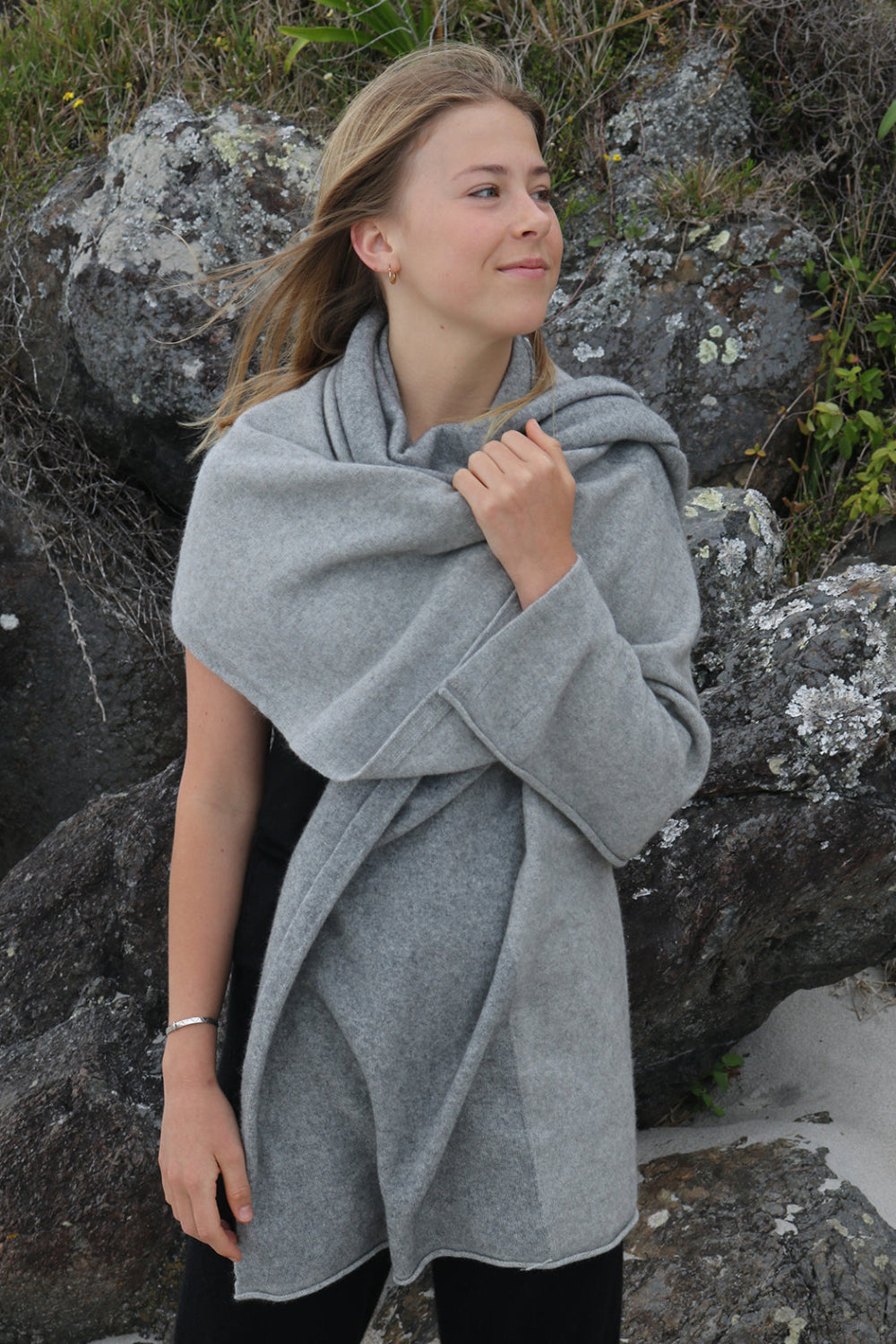 A woman standing outdoors wearing a gray Merinosilk travel wrap that is draped over her shoulders.
