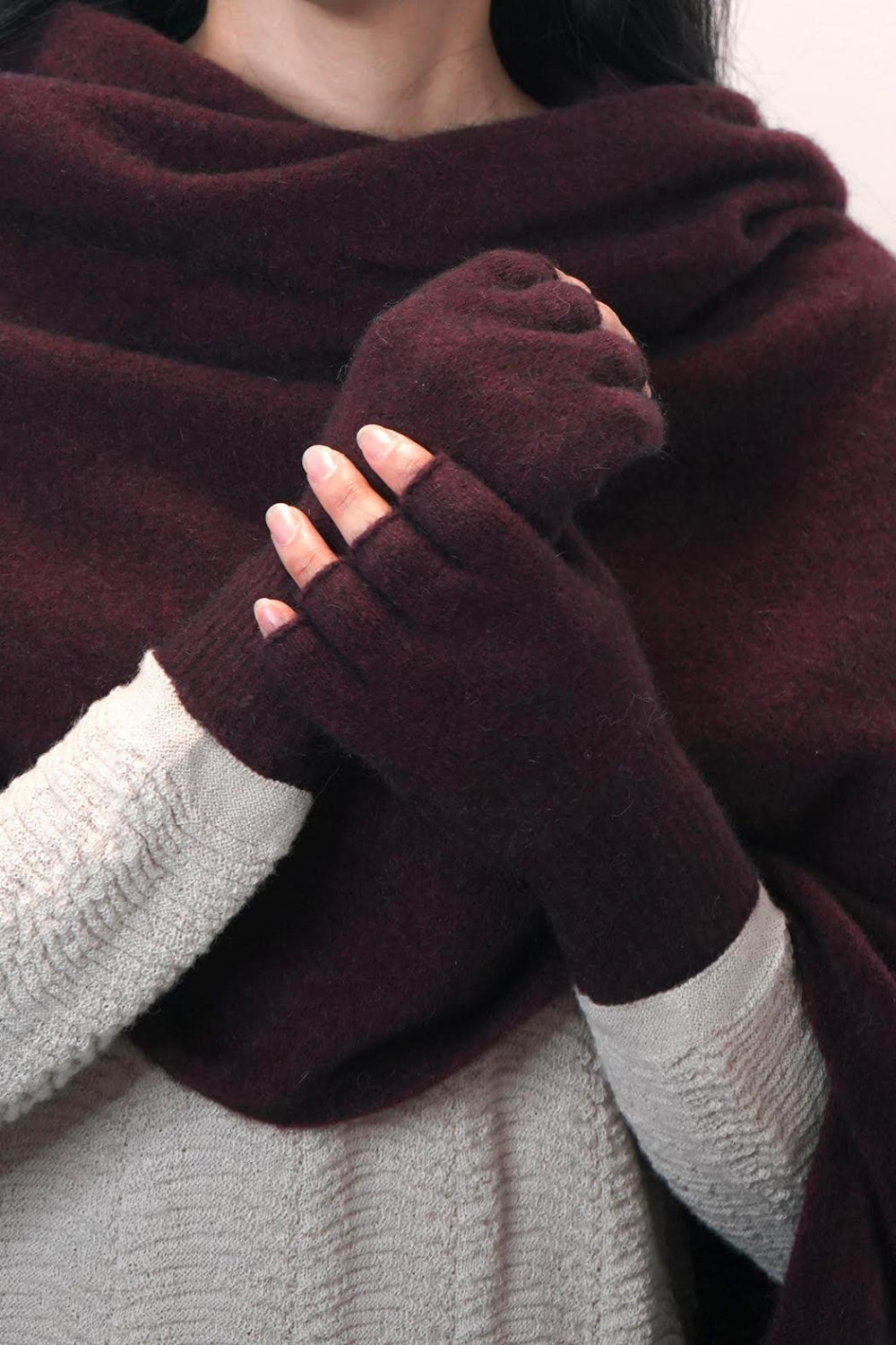 A pair of merino fingerless gloves in red, being worn by a person.