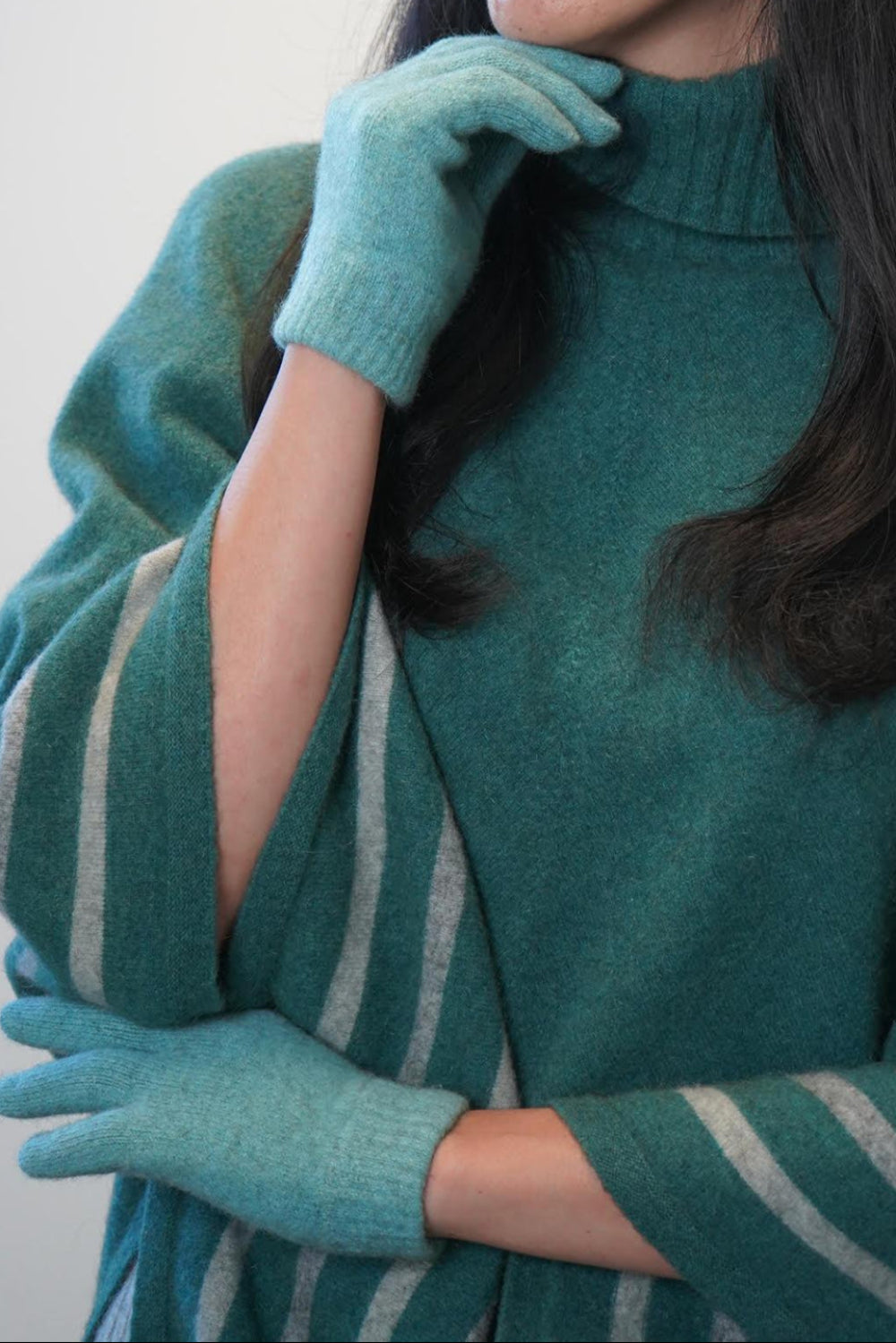 Person wearing a teal sweater and matching gloves against a white background