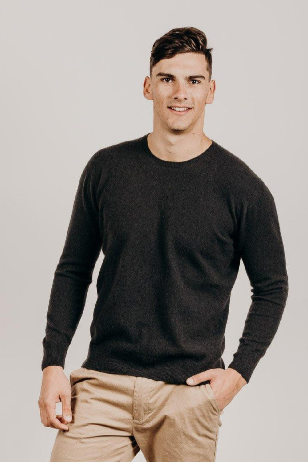 Man wearing a dark color sweater and beige pants against a plain background