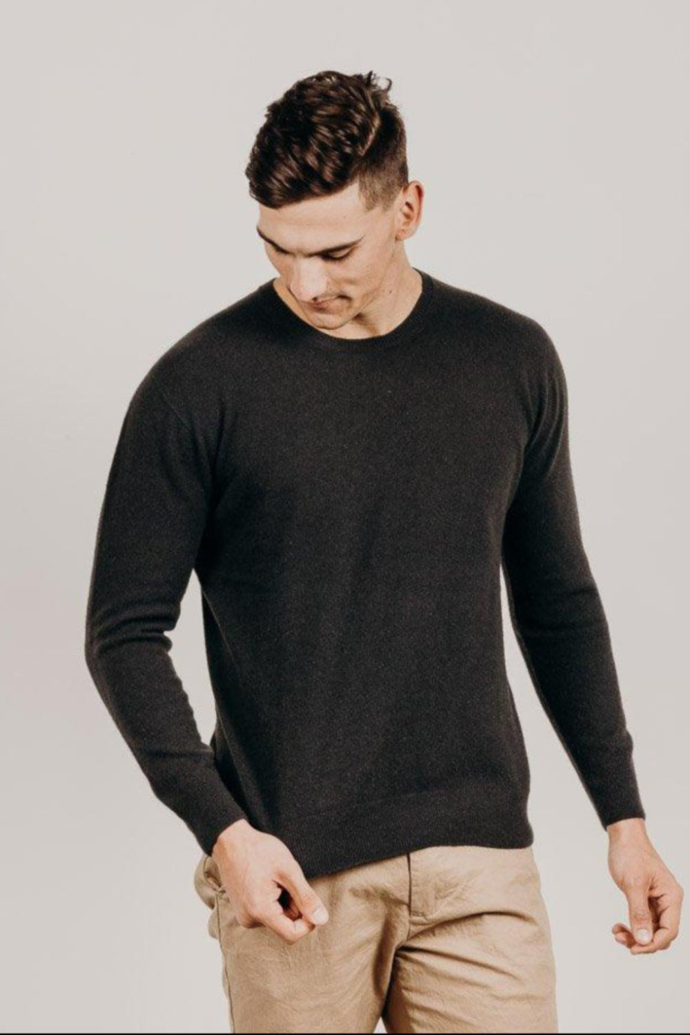 Man wearing a black sweater and beige pants against a plain background