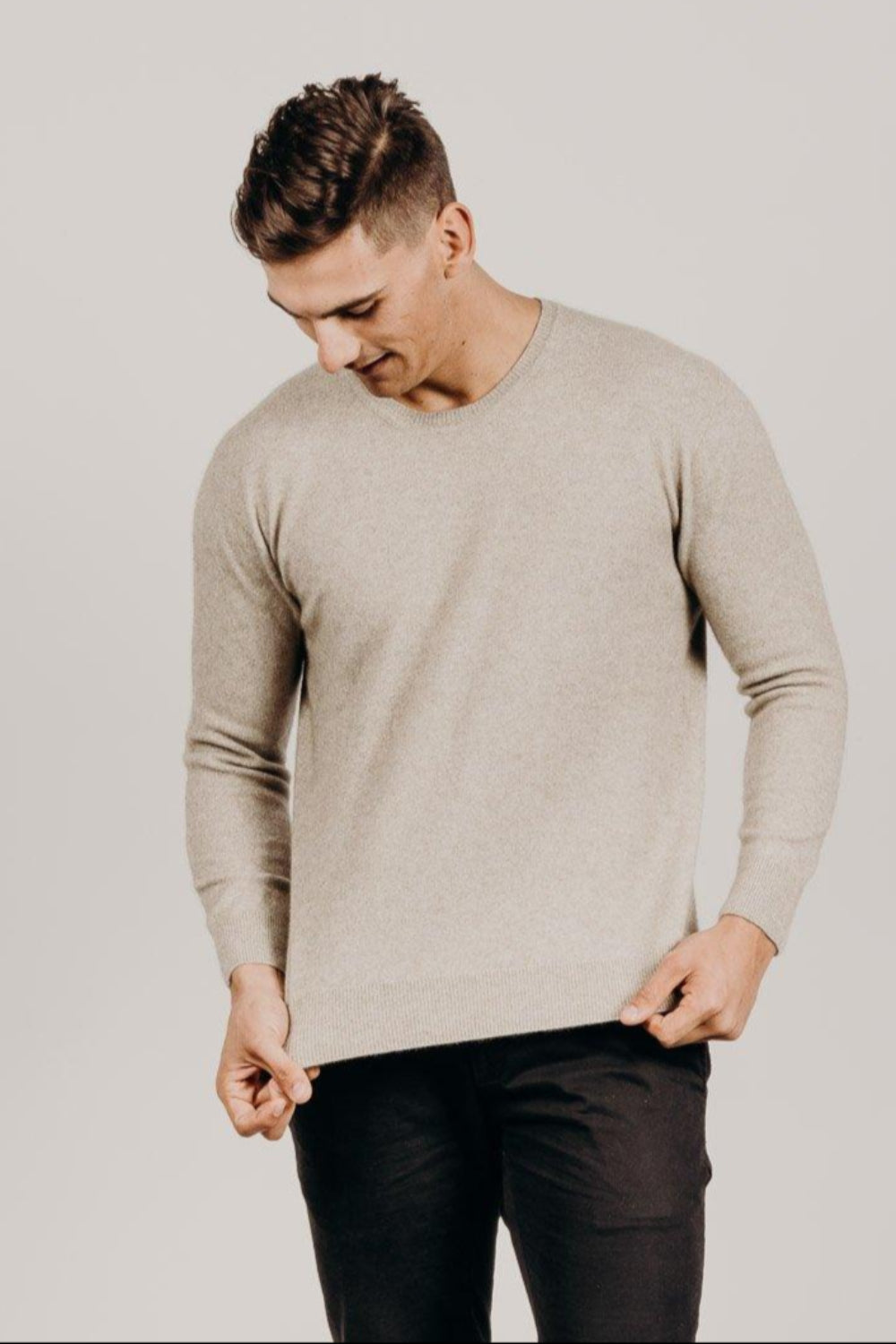 Man wearing a beige sweater and black pants against a plain background