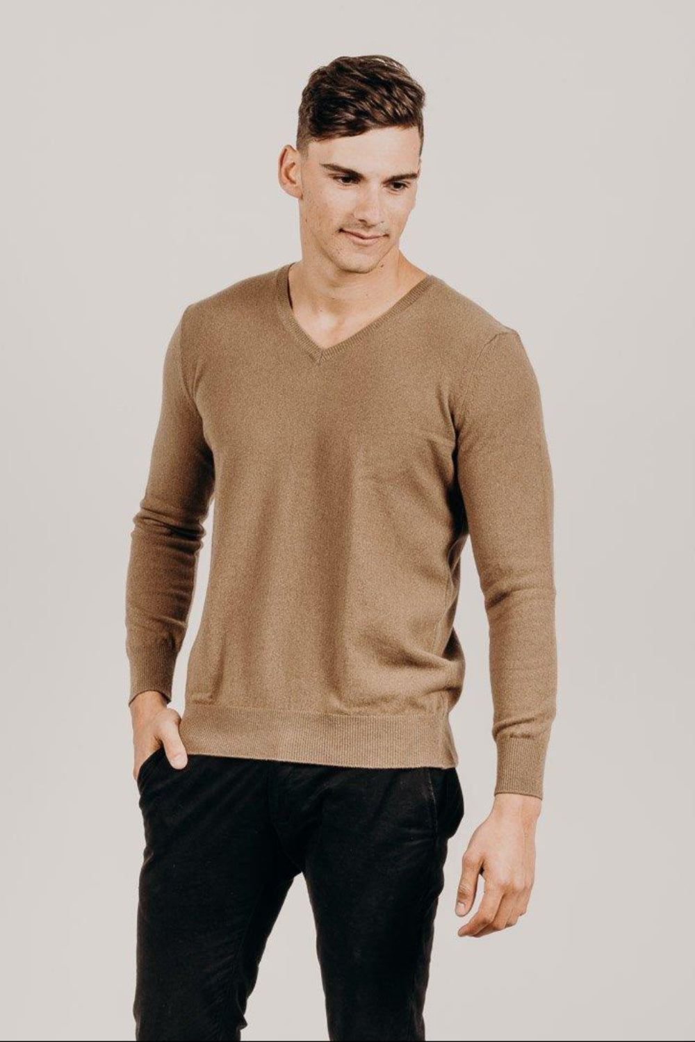 A man wearing a beige V-neck sweater, which appears to be made of a fine, luxurious fabric.