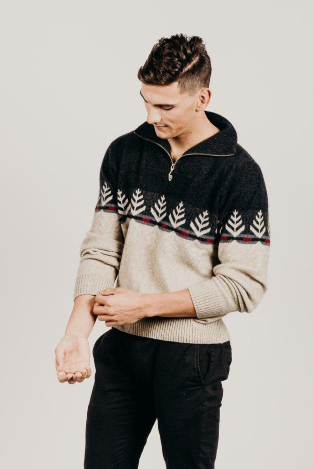Man wearing a black and beige patterned sweater against a plain background