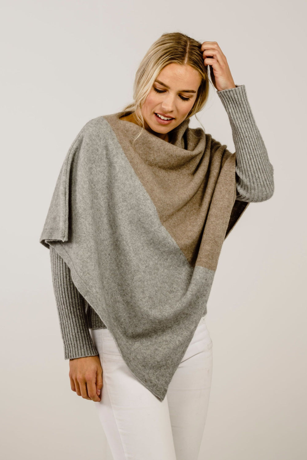 Woman wearing a two-tone poncho with gray and beige colors on a plain background