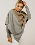Woman wearing a two-tone poncho with gray and beige colors on a plain background