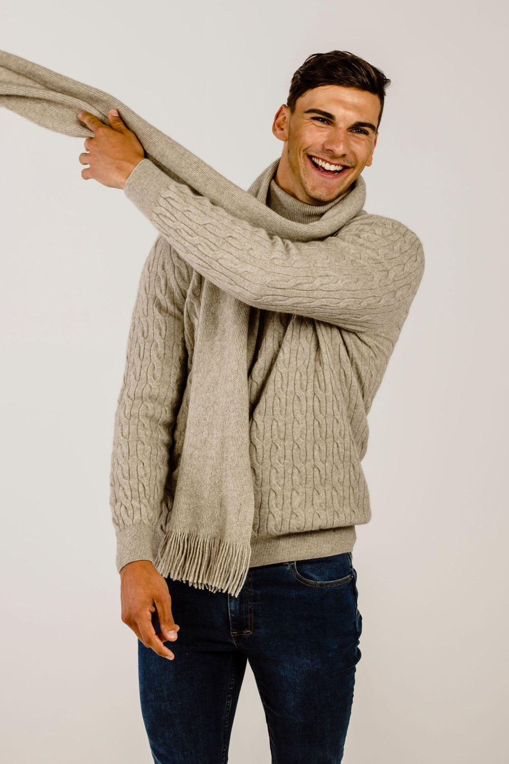 Man wearing a beige sweater and scarf against a plain background