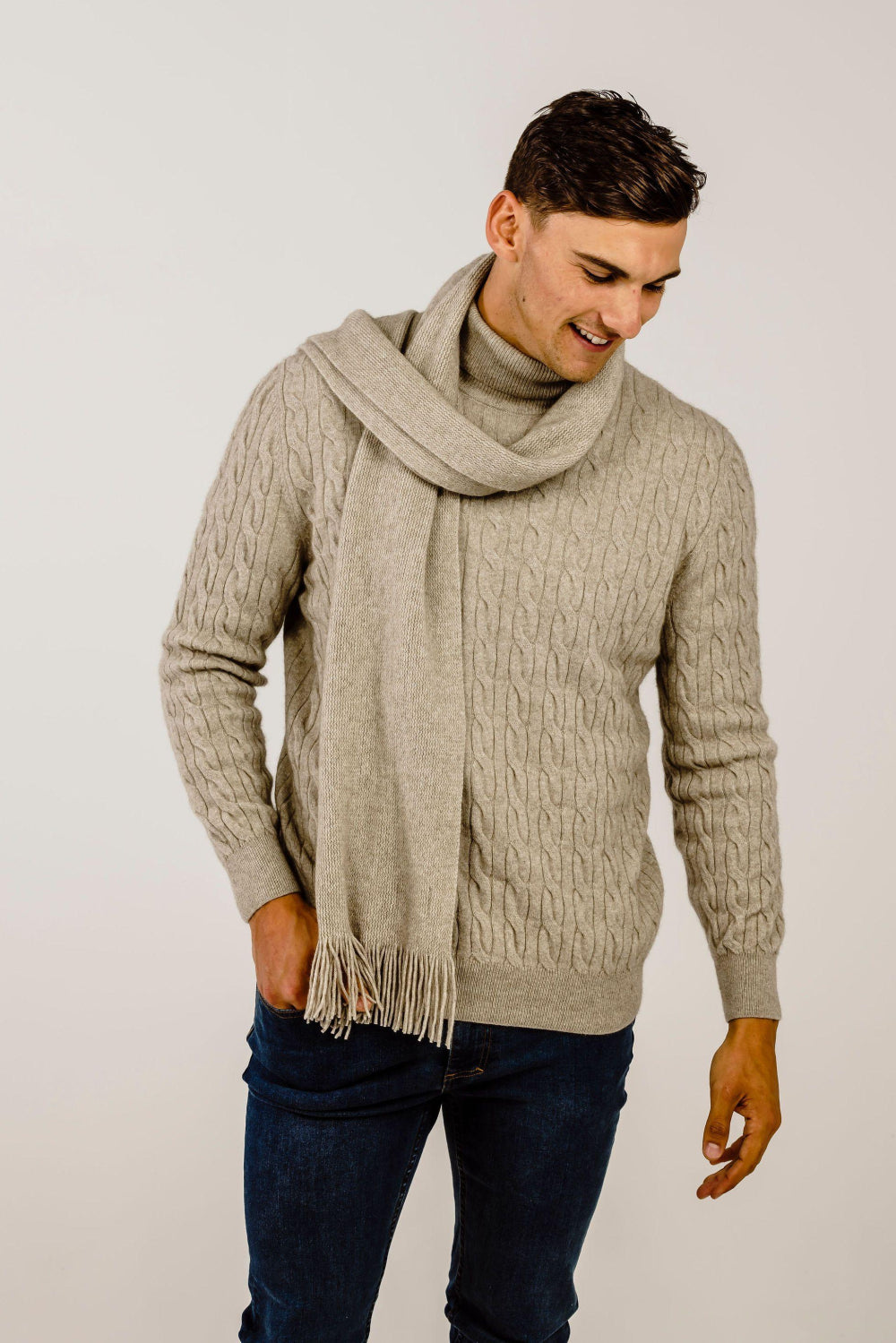 Man wearing a beige sweater and scarf against a plain background