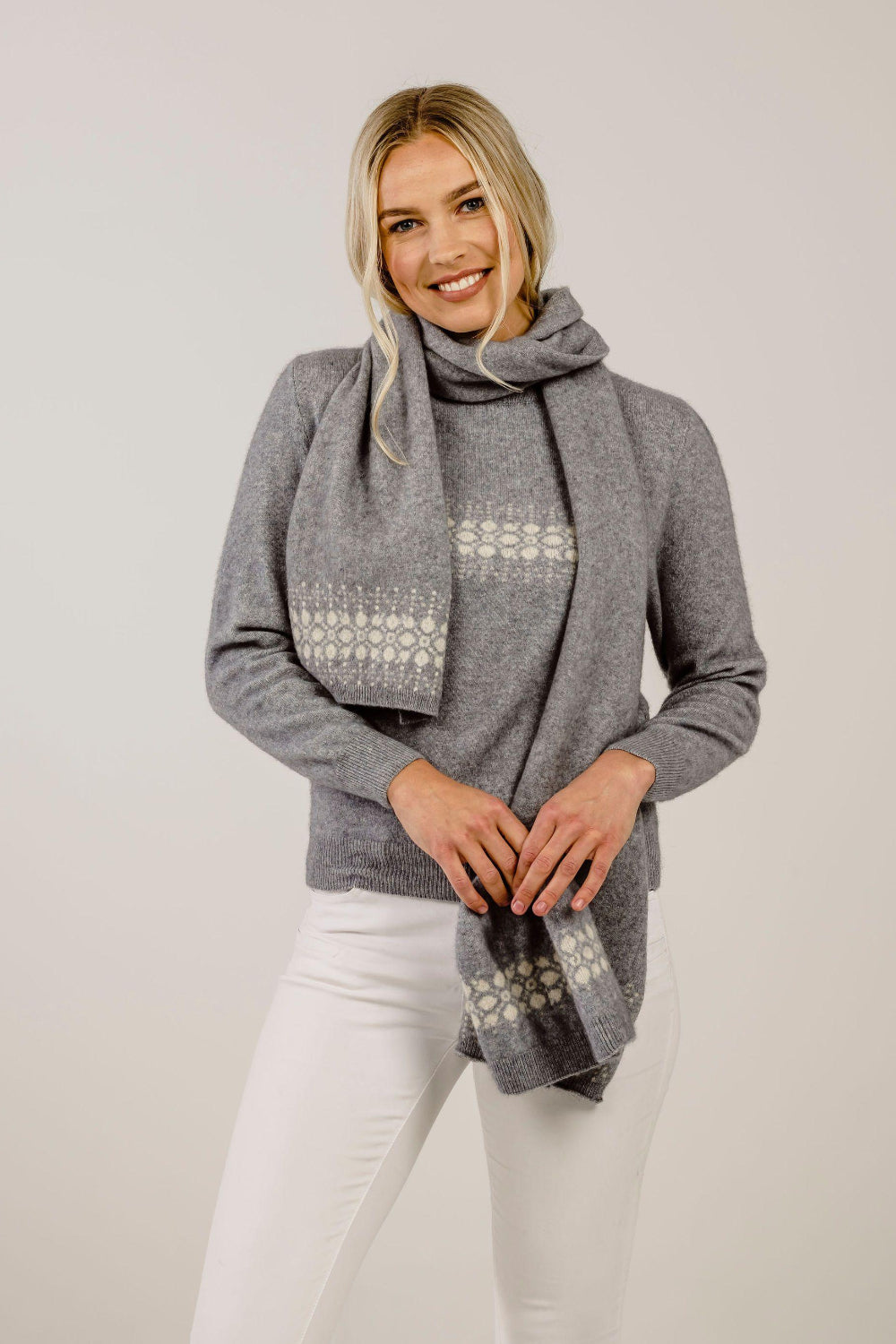 Woman wearing a gray sweater and patterned scarf against a plain background