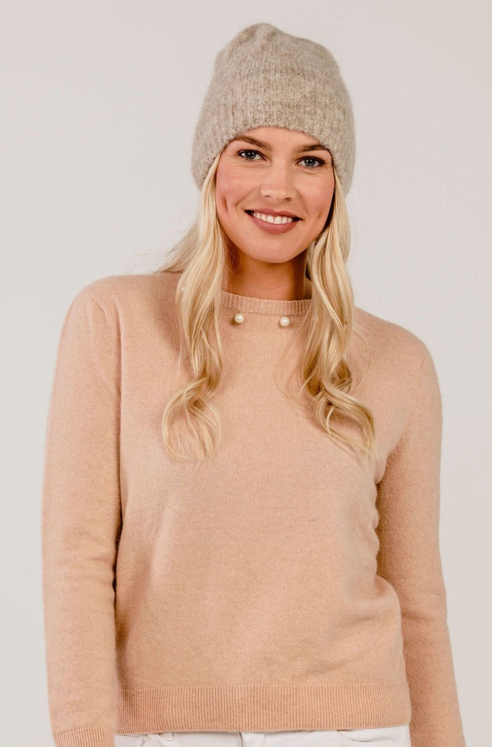 Woman wearing a pink sweater and knit beanie on a plain background