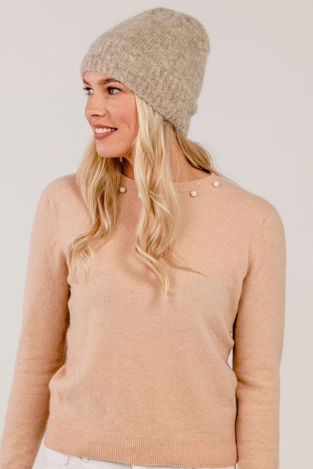 Woman wearing a beige knit beanie and sweater against a plain background