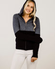Woman wearing a grey and black  hoodie on a plain background
